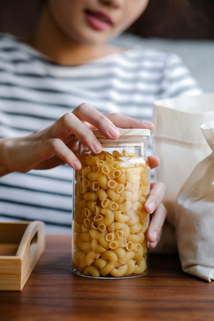 female with sustainable glass jar filled with pasta on wooden table in kitchen. Best Tips For An Eco Friendly Kitchen