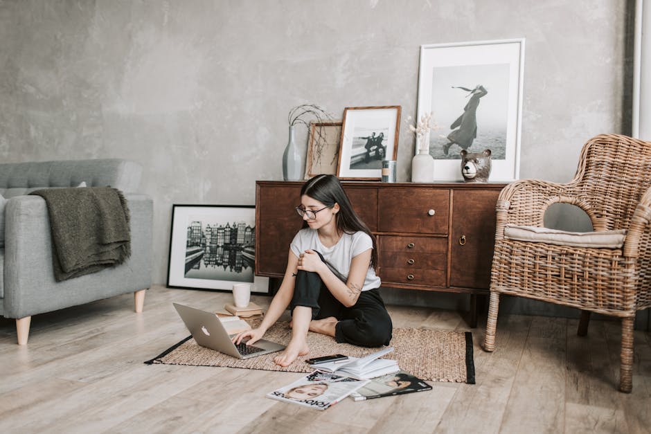 Smiling female in casual clothes and eyeglasses reading netbook while sitting barefoot on floor carpet. Representing a Shopping Guide For An Eco-Friendly Home